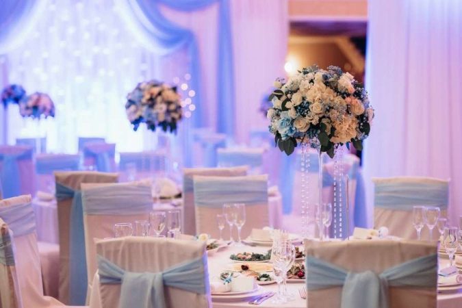 Salle de mariage décorée en bleu et blanc avec hauts vases floraux et chaises à nœuds, dans un lieu de réception élégant et romantique.