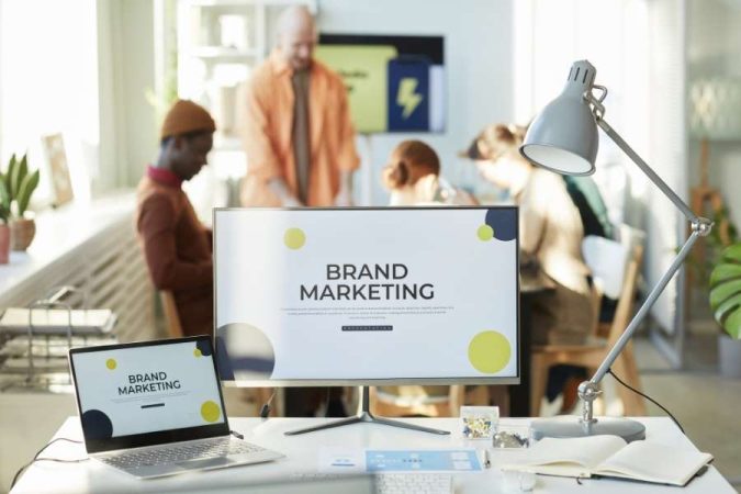 Un écran d'ordinateur et un ordinateur portable affichent une présentation de brand marketing dans un bureau moderne et lumineux.