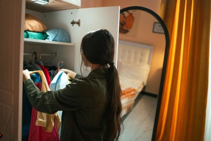 Une jeune femme prend des vêtements dans son dressing pour organiser ses placards efficacement.