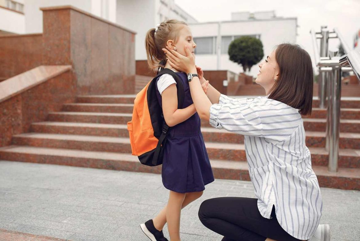 Mère préparant sa fille avec son sac à dos devant sa nouvelle école suite à la fourniture des pièces justificatives pour inscription école suite à un déménagement.