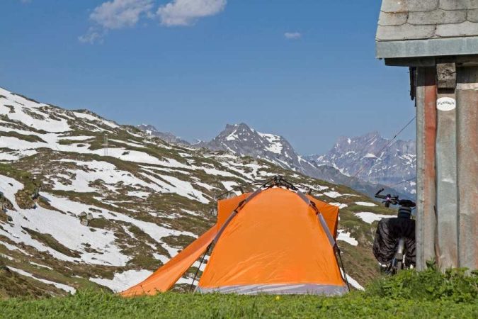 Une tente orange installée en montagne démontre l'équipement pour un bivouac réussi face à des sommets enneigés.