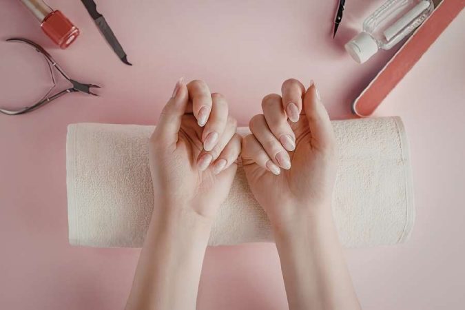 Des mains posées sur une serviette pour une manucure maison longue tenue.