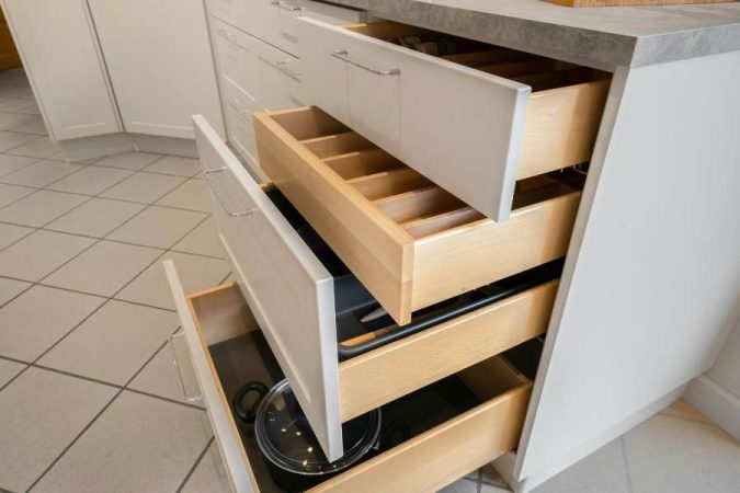 Plusieurs grands tiroirs en bois de cuisine sont ouverts en cascade, révélant des compartiments de rangement et des ustensiles.